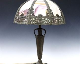 An early 20th century American bent panel table lamp.  Cast filigree shade with Purple and Amber Slag Glass panels on a stylized cast base and circular foot with patinated finish.  Some wear to patina, repair to top Bronze rim inside shade, sockets replaced.  23" high.  