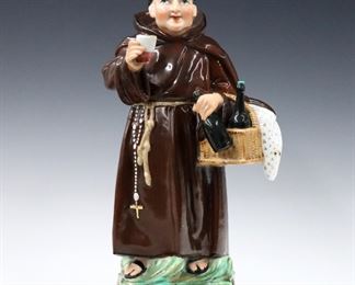 A turn of the century Portuguese porcelain brandy warmer in the figure of a monk.  Depicted toasting while holding a basket of wine bottles with polychrome decoration and Gilded detail.  Two-pieces with upper mug and lower warming compartment.  Impressed "V" at underside.  Minor wear to painted decoration.  12" high.  
