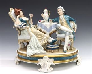 A mid 20th century Royal Dux "Afternoon Tea" porcelain figural grouping.  Depicts a lounging couple having tea on a scrolled Rococo style base with polychrome decoration and Gilded detail.  Printed "Royal Dux" mark.  Slight wear to decoration.  Approx. 15 x 10 x 12 1/2" high overall.  

