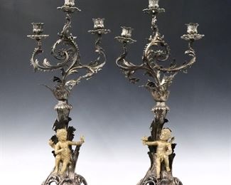 A pair of 19th century Rococo style silvered candelabra.  Three light design with two foliate arms over a scrolled base with silvered finish and Gilded putti figures. 