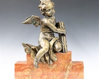 A turn of the century French Bronze figure of Cupid.  Depicted seated with flowing robe and bundle of wood to fashion arrows on a stepped Red Marble base.  