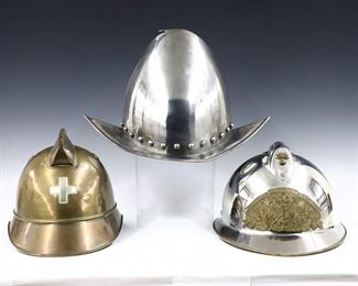 Three 19th to mid 20th century helmets.  Includes a Brass Swiss fire helmet with raised comb and cross, a French polished Steel fire helmet with raised comb and Brass shield, and a Steel Spanish Morion style helmet with pointed brim and high crest.  