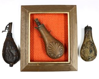 Three 19th century powder flasks.  Includes two of Brass with embossed shell design, one custom mounted in a wooden frame, and one of leather with embossed hare and fowl design.  Some wear, oxidation and denting, leather with losses.