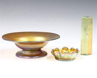 Three pieces of early 20th century Art Glass.  Includes a Louis Comfort Tiffany Favrile glass footed bowl and ruffled salt cellar, with a prism form knife rest.  Each Iridescent Gold with Pink/Purple sheen.  Bowl incised "L.C. Tiffany Favrile" and cellar "L.C.T. Favrile", knife rest unmarked.  Minor surface wear, small edge flakes to prism.  Up to 6" diameter.  