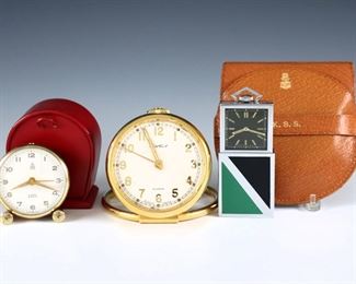 Three early to mid 20th century travel alarm clocks.  Includes a cased Brass Cartier 8-day clock with Swiss movement, a cased Brass Mark Cross 8-day clock with Swiss movement, and a chrome Ingersoll clock with enameled Art Deco design.  