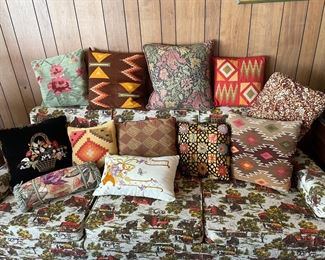 A variety of throw pillows made from antique textiles including wool rugs, embroidered pieces, and fine prints