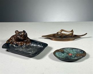 (3PC) TABLE ITEMS  |  Including a bronze leaf-form dish stamped" R. Schumacher" (7 in.), a bronze ashtray with verdigris (4 in.), and a white metal ashtray with a painted bear head (5.5 in.)