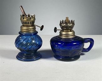 (2PC) PAIR HONG KONG BLUE GLASS OIL LAMPS  |  Made in Hong Kong, one lamp with fruit reliefs and handle in cobalt blue, the other with a swirled glass body.