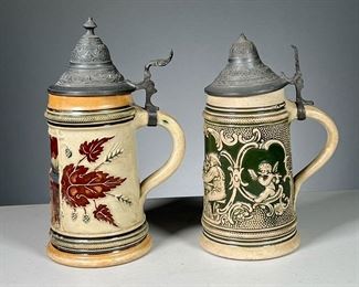 (2PC) GERMAN STEINS  |  Both stamped “Germany” on the bottom and with pewter hinged lids, including a half liter “Wohlbekom” stein and a smaller green stein
Dimensions: w. 5 x h. 8 in (tallest)