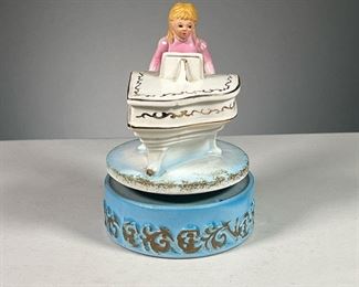 GIRL ON PIANO MUSIC BOX  |  Designed as a girl in pink dress playing a gilt piano on a blue stage. Dimensions: h. 6.75 x dia. 4 in