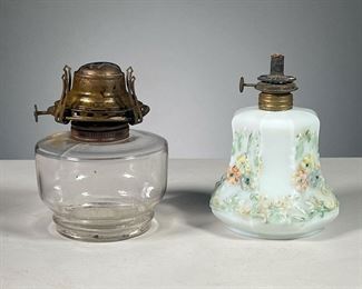 (2PC) GLASS OIL LAMPS  |  Small lamps, including a clear glass oil lamp and a white milk glass oil lamp with raised floral painted decoration. Dimensions: h. 6 x dia. 4 in (Largest)