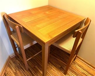 Vintage Teak High Top Table and Two Stools with Woven Seats. This table set is in very good condition and features a "hidden" retractable leaf. 

Item measures 35.5" x 35.5" x 37"