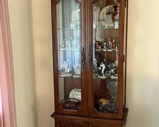 curio cabinet with Hummels, Norman Rockwell figurines, cranberry glass vase, Campbells soup mug, crystal, and other items
