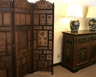 Four panel carved screen from India next to a hand painted sideboard. Pai of Chinese Famille noir lamps.