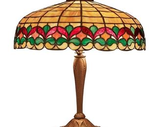1190
Early 20th century; Brooklyn, NY
A Wilkinson Leaded Glass Table Lamp
Shade and base not marked
The leaded glass, skirted dome shade with a stylized iris flower band and scalloped edge in hues of yellow, red, and green on a two-light patinated metal base with floral motifs and a concentric circle patterned foot, electrified
Overall: 21" H x 18.75" Dia.
Estimate: $800 - $1,200