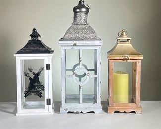 (3PC) DECORATIVE LANTERNS | Tallest Lantern with white Wood and a silver-toned metal top. Unfinished wood with gold toned metal top; and white wood with black metal top, with "Merry Christmas" reindeer decoration on glass. - l. 9 x w. 9 x h. 24 in (White Lantern with Silver top is Tallest)