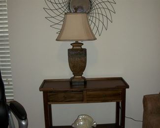Wood 2 Drawer Entry Table, Table Lamp, Metal Wall Art with Mirror in center.