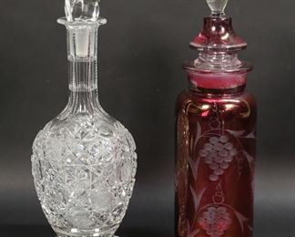          4	2 Decanters Cut Glass & Cranberry Glass	2 glass decanters. Cut glass decanter, with mismatched stopper, 11 5/8"H; cranberry glass decanter with etched grape decoration, 11 7/8"H. Cut decanter minor chips and fleabites throughout, chips to stopper and interior end of stopper; cranberry decanter losses to color around rim and larger stopper, chips to interior end of smaller stopper.
