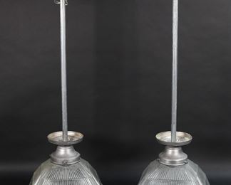        181	Pair of Holophane Hanging Fixtures	Pair of hanging pendant lights with square signed Holophane glass shades. Each 30 1/2"H including hardware, shades 11 3/8" x 11 3/8" at bottom, 4"-diameter at top. Large chip to rim of one shade under fitting, minor chips to each shade, hardware and caps bent, scratched and with paint residue.
