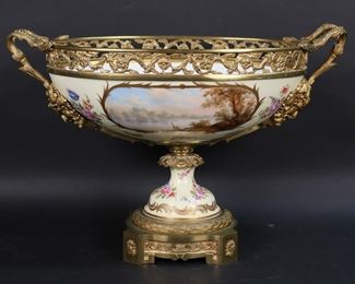        278	Sevres Style Porcelain Centerpiece	Sevres style porcelain centerpiece. Hand painted with courting scene on one side and landscape on the reverse, gilt enameled decoration, with gilt bronze mounts and figural gilt bronze Satyr handles. Unsigned. 18 1/4"L x 12"H. Crack to porcelain base just below mount.
