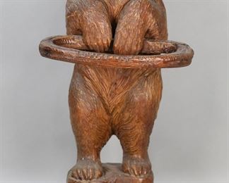        312	Carved Black Forest Bear Umbrella and Cane Stand	"Carved Black Forest bear umbrella and cane stand. Late 19th century. Carved bear with glass eyes holding carved ring. Inset metal tray on base of stand. Large vertical splits and cracking to wood left side of bear's head and throughout left side of body. Repairs to carved ring-form holder. Holder is loose in place. Wear and tarnishing to metal tray. Abrasions and scuffs to wood on back of bear. Scuffs, chips, and wear throughout wood of base. 

11 5/8"" W x 12"" D  x 26"" H. 19 lbs."
