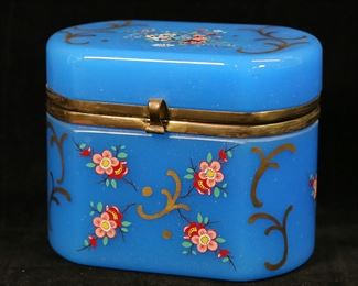        332	Hand Painted Blue Opaline Glass Dresser Box	Blue opaline glass dresser box or scent casket. Hand painted with floral and gilt decoration. 5 3/8"W x 3 1/2"D x 4 1/4"H. Minor losses to gilt and flower decoration, losses to brass patina on mounts, flakes and roughness to interior rims of lid and box.

