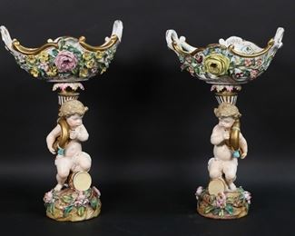        338	Pair of Bevington Porcelain Cherub Compotes	Pair of figural compotes or centerpieces. Cherubs with horns, applied floral decoration. Blue John Bevington JB with swords mark to the underside of one. Taller, 13 3/4"H x 8 5/8"W at handles. Chips and losses to flowers on both, repair to one below basket, chips and roughness to decoration below baskets on both, interior of basket of one with roughness, imperfections and discoloration.
