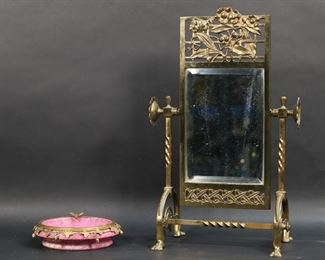        374	Brass Mirror & Marble Ashtray	Lot of 2 tabletop items. Brass swivel table mirror, with openwork floral decoration, 10 5/8"W x 17"H; pink marble ashtray with gilt metal leaf decoration, 6 1/4"-diameter. Mirror minor losses to brass patina, scratches to mirror.
