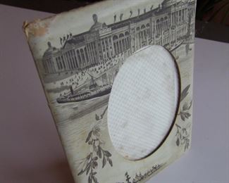 Lot 011   1893 Souvenir World's Fair pressed & formed lithographic paper picture frame includes a Battleship image and the Grand Basin with Agricultural Building 6" x 8 1/2" h. (for a 4" x 5" photo).  Cond:  Moderate wear around edges, kick leg has taped repair.         Est. $40-60.