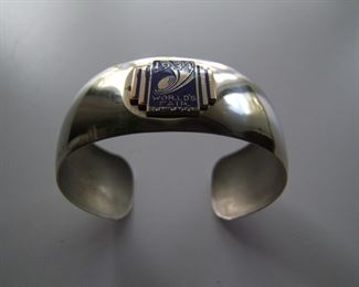 Lot 037   1934 World's Fair Ladies Bracelet, enameled copper Deco medallion on a rounded sheet nickel band, 1" wide x 2 1/2" dia. (widest point).  Cond:  Excellent cond., never worn.  Est. $50-80.