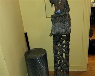 sculpture a carved figure playing percussion instrument with burlap clothes and encrustation.