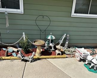 More lawn art/garden art including what appears to be a wait for hitching horses three piece alligator, scent bird bath, and non-cement kids on the TV totter, 2 cement frogs courting on a cement bench under the umbrella, a (cement) bird on top of a (cement) stump, a Chinese pagoda, water, hoses, and a donkey pulling a wagon ( both are cement) and some shepherd hooks in the back ground.
