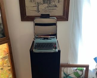 This is a better picture of the typewriter sitting on top of the stereo speaker.  There is a framed stained glass of hummingbirds to the right, slightly behind the Route 66 sign.