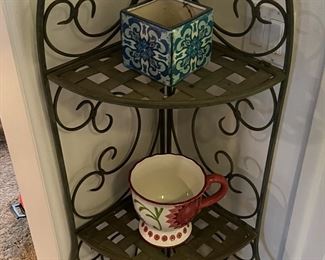 Here you see a wrought iron corner shelf unit expertly displaying three decorative vases or cups.