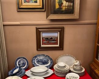 Fine dishware of various styles are on the table while on the wall are three framed artworks.