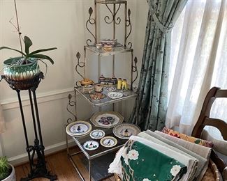 metal and glass 4-tier corner shelf (2 available), Quimper pottery, metal and wood plant stand, metal wall sculpture, and dining table runners