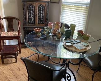 Asian wood armchair with stool, 1920's circa tall carved storage chest, antique martinet string puppets, Roseville and Pewabic pottery on top of a round glass table with a metal base and 3 leather and metal dining armchairs
