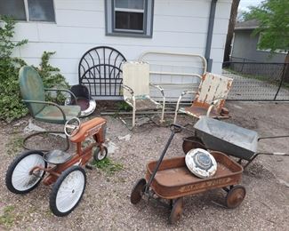 Outdoor items including metal bed frames, metal chairs, old toy tractor, old radio flyer wagon and a galvanized metal wheel barrow