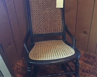 This sewing rocker features a caned seat and back. A hand-written notes shares the history of the chair. 