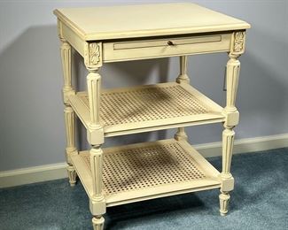 CANE SIDE TABLE | Three tier end table in white/cream paint with two caned shelves and a pullout shelf / writing surface on top with floral carvings in the corners and spindle carved legs. - l. 22 x w. 19 x h. 29 in