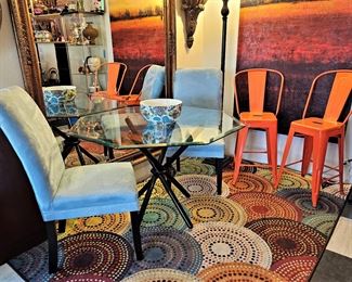 Vintage octagon glass table. Black metal legs. 2 light blue side/dining chairs. New rug and 2 orange metal bar height stools.