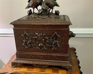 A carved walnut liquor cabinet, topped with a pair of quails surrounded by their clutch nestled in foliage, the handles on each side are in the form of bear heads, and the front is a beautifully rendered wreath of maple leaves and vines.