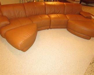 Item 2: Two-piece modern brown (cognac color) curved leather sectional sofa with adjustable backs and with (2) rolling ottomans. Brand name not found. Each section measures 65” wide x 42” deep x 30” tall. Each ottoman measures 40” wide x 25” deep x 18” tall. PRICE: $1,895.00