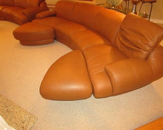 Item 2: Two-piece modern brown (cognac color) curved leather sectional sofa with adjustable backs and with (2) rolling ottomans. Brand name not found. Each section measures 65” wide x 42” deep x 30” tall. Each ottoman measures 40” wide x 25” deep x 18” tall. PRICE: $1,895.00