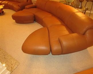 Item 2: Two-piece modern brown (cognac color) curved leather sectional sofa with adjustable backs and with (2) rolling ottomans. Brand name not found. Each section measures 65” wide x 42” deep x 30” tall. Each ottoman measures 40” wide x 25” deep x 18” tall. PRICE: $1,895.00