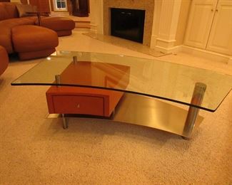 Item 3: Contemporary stainless, wooden, and glass top cocktail table with drawer. Brand name not found. 57.5” wide x 29” wide x 16.5” tall. PRICE: $650.00