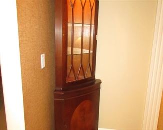 Item 12: Lighted bowfront corner cabinet with inlay. Not marked with brand name. 73” tall x 18” deep. 25” from each back corner to front. PRICE: $575.00