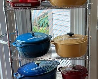 Chrome Storage Rack with several Dutch Ovens from LeCreuset, Martha Stewart, Amazon Basic and Cuisinart as well as several stoneware items from LeCreuset on top two shelves
