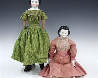 Two 19th century dolls. China heads with molded hair and painted detail, on cloth jointed bodies. Includes an "Adalina Patti" doll with porcelain lower arms and legs with heeled boots and Brown painted hair wearing a Pink floral dress with lace, and a doll with cloth arms and legs with Brown painted "flat top" hair wearing a Green printed dress. Minor wear to paint, fabric with some fading and staining, Adalina Patti with repaired break to one leg. Up to 20 1/2" long. ESTIMATE $50-100