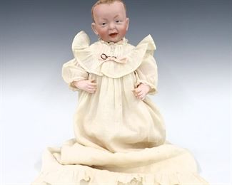 A turn of the century Kammer & Reinhardt Model 100 "Kaiser Baby" doll. Bisque socket head with molded features and painted detail, on a jointed composition body. Wearing a linen and lace Christening gown with knit booties. Impressed "K R" mark with Star. Some wear, painted touch-ups to hands and feet. 14 1/2" long. ESTIMATE $100-150